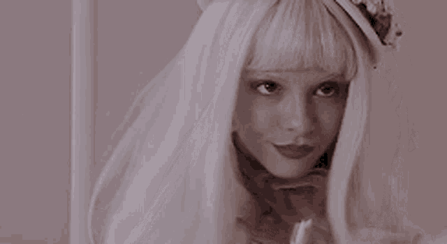 a woman wearing a white wig and a flower headband is smiling with her eyes closed .