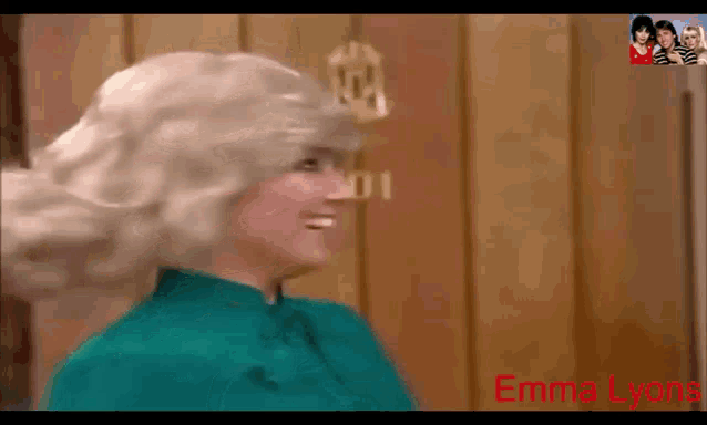a woman in a wig is standing in front of a door that says emma lyons