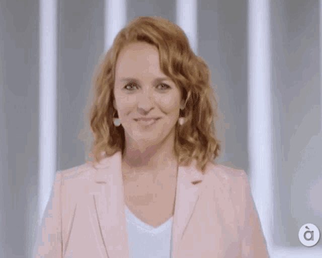 a woman in a pink jacket is smiling in front of a sign that says à