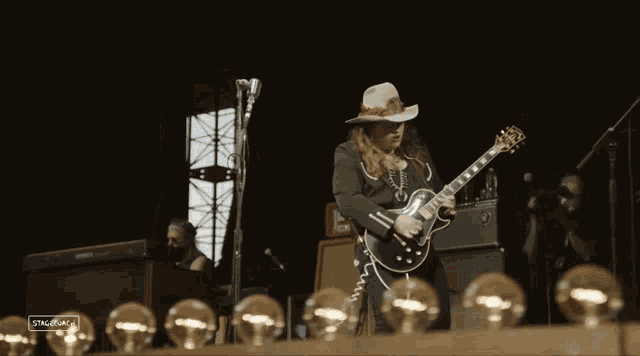a man in a cowboy hat is playing a guitar and singing into a microphone on stage