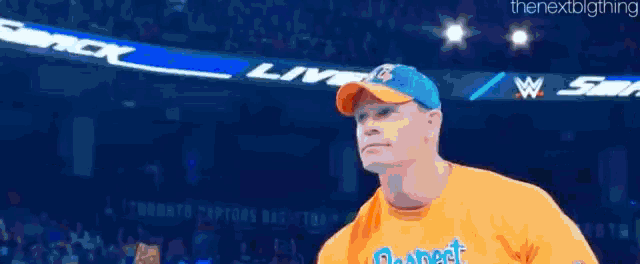 a man in an orange shirt is holding a microphone in a ring .