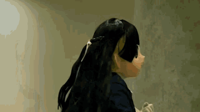a doll with long black hair is standing in front of a concrete wall .