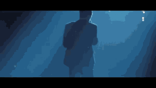 a man in a suit is standing in front of a blue light .