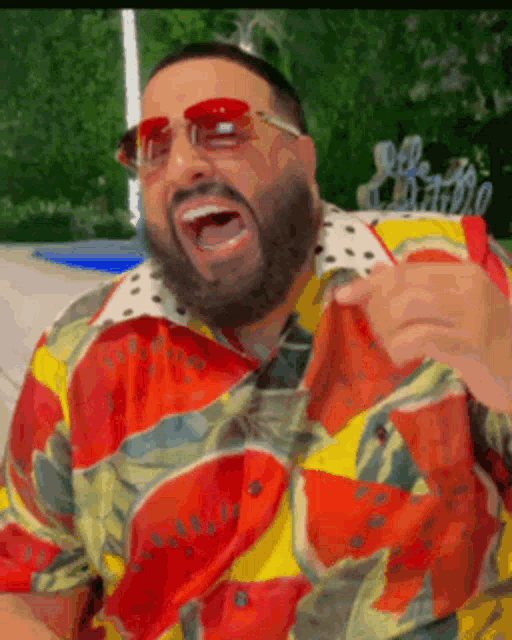a man wearing sunglasses and a watermelon shirt is laughing with his mouth open