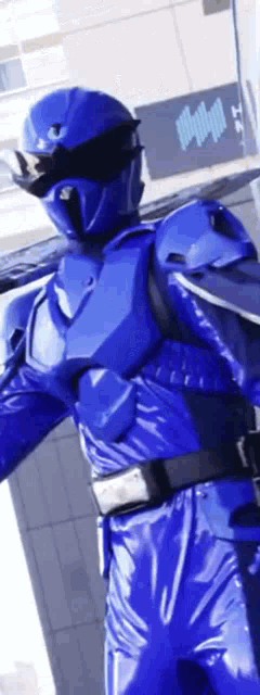 a blue superhero is standing in front of a building holding a sword .