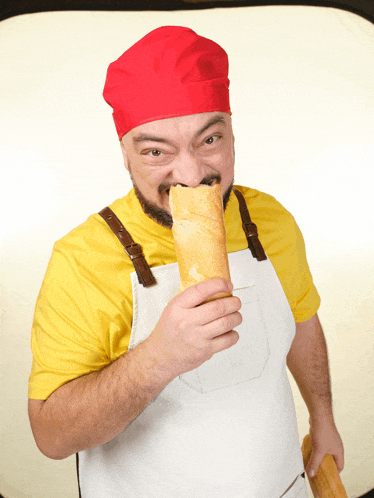 a man wearing a yellow shirt and an apron is eating a loaf of bread