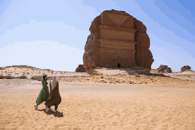 a woman in a green dress walks with a man in a brown robe in the desert