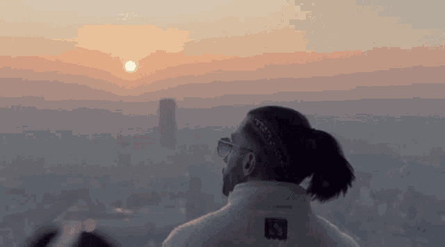 a man in a ponytail looks at the sun setting over the city