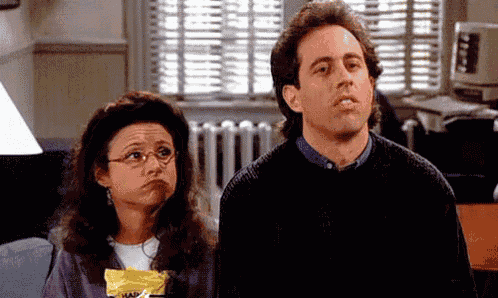 a man and a woman are sitting next to each other in a living room . the woman is holding a bag of chips .