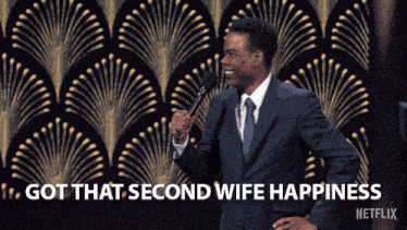 a man in a suit and tie stands in front of a microphone with the words " got that second wife happiness " above him