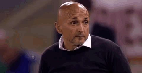 a bald man with a beard wearing a black sweater and a white shirt is looking at something .
