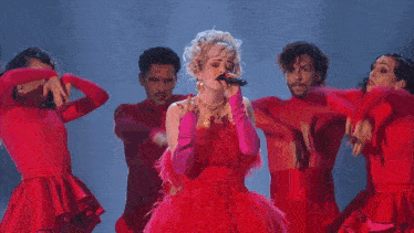 a woman in a pink dress singing into a microphone with two men behind her