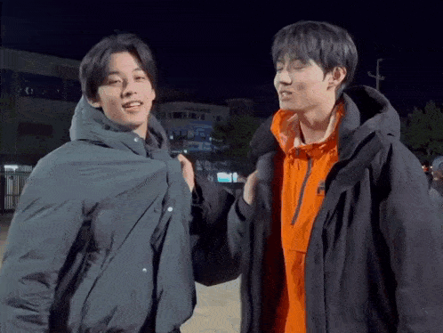 a couple of young men are standing next to each other in jackets .
