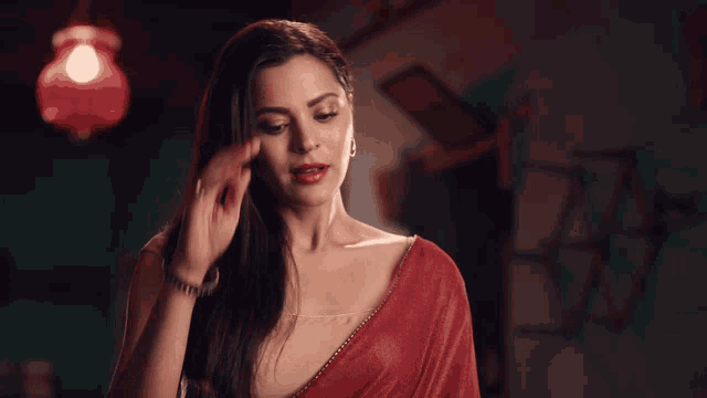 a woman in a red saree holds her hand to her forehead