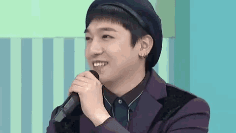 a young man in a purple suit and beret is holding a microphone in his hand .