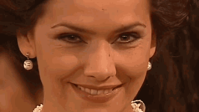 a woman wearing a pearl necklace and earrings smiles