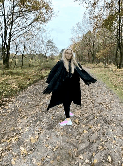 a woman in a black coat and pink sneakers is standing on a dirt road .