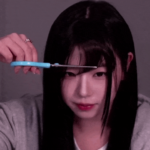 a woman is cutting her hair with a pair of scissors .