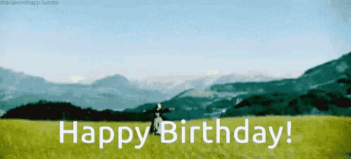 a woman is standing in a field with mountains in the background and says happy birthday .