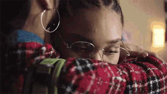 a woman wearing glasses is hugging another woman who is wearing a plaid shirt .