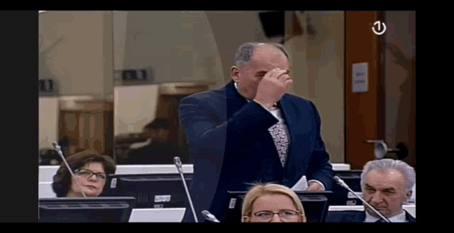 a man in a suit and tie wipes his nose while sitting in front of a microphone .