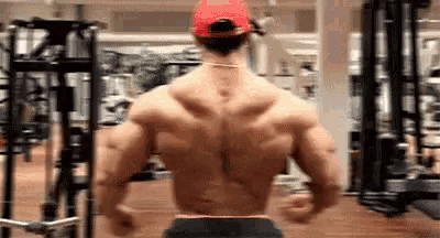 a man is standing in a gym with his back to the camera and wearing a red hat .