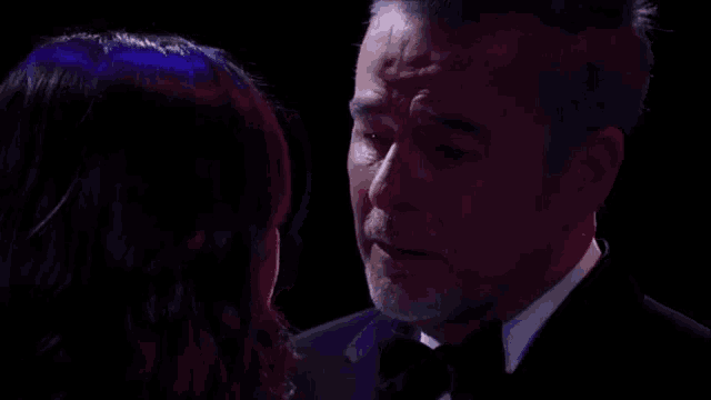 a man in a tuxedo is crying while looking at a woman in a dark room .