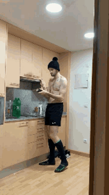 a shirtless man is standing in a kitchen with a bottle of sprite in the background