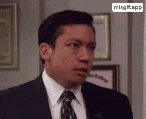 a man in a suit and tie is looking at the camera with a misgif.app icon behind him