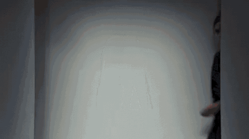 a person is standing in a dark room with a white wall behind them .