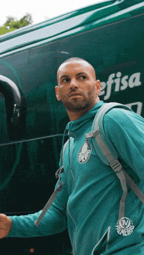 a man wearing a green palmeiras jacket walks in front of a bus