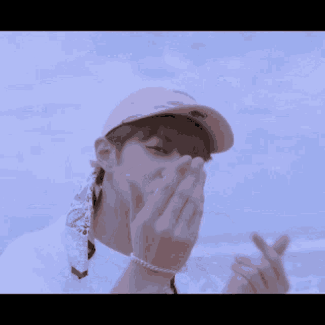 a young man wearing a pink hat and a white shirt is making a heart shape with his hands .