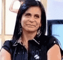 a woman wearing a black shirt and earrings is looking at the camera .