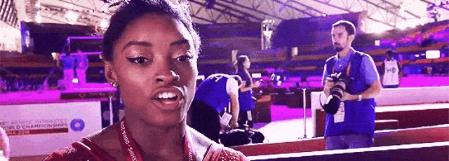 a woman is talking to a cameraman in a stadium while a man takes a picture of her .