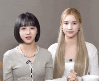 two women are sitting next to each other and one has a necklace that says ' x ' on it