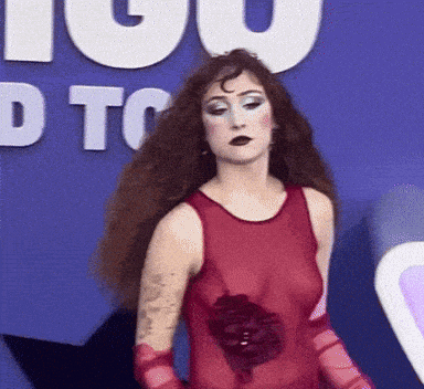 a woman in a red dress and red gloves stands in front of a sign that says " you "