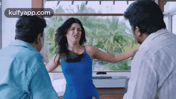 a woman in a blue dress is standing between two men in a living room .