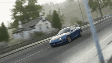 a blue car is driving down a road in front of a white house