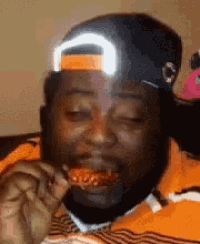a man wearing an orange nike hat is eating a piece of pizza