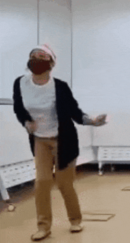 a woman wearing a face mask and a hat is dancing in a room .
