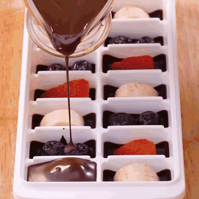 chocolate is being poured into an ice cube tray with fruit