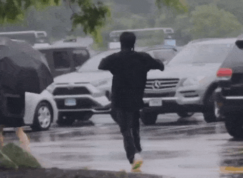 a man in a black shirt is running through a parking lot with umbrellas .