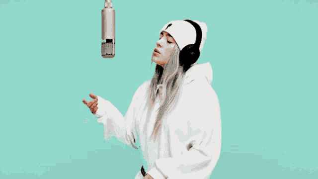a woman wearing headphones and a beanie sings into a microphone