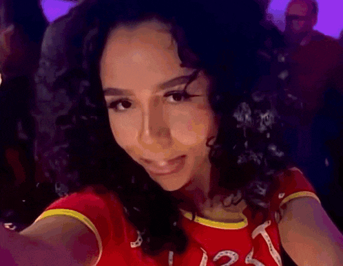 a woman with curly hair is wearing a red shirt with a yellow stripe that says t.
