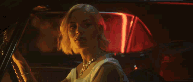 a woman in a white dress is driving a car with red lights behind her