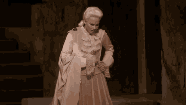 a woman in a white dress is standing in a dark room with stairs in the background