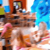 a blurry picture of children sitting at tables with a blue monster behind them