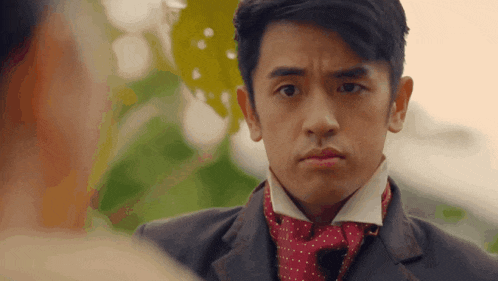 a man wearing a suit and a red scarf looks at another man