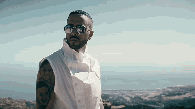 a man with a tattoo on his arm is wearing sunglasses and a white shirt