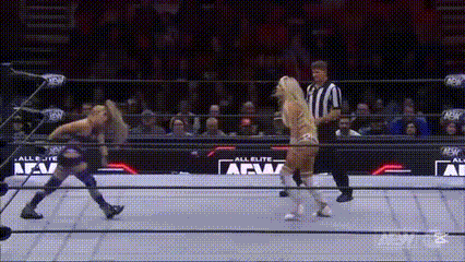 two women are wrestling in a ring with a referee standing behind them .